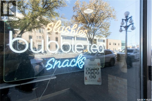 Close-up of a window with neon signs reading "slushies, bubble tea, snacks". - 45 High Street W, Moose Jaw