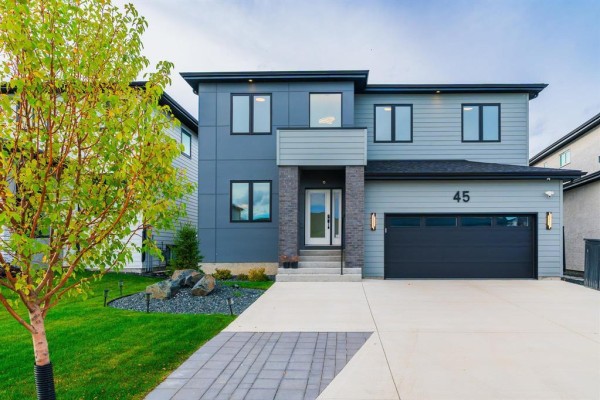 Front view of a modern grey house with a large tree and landscaping. - 45 Karschuk Bay, Winnipeg