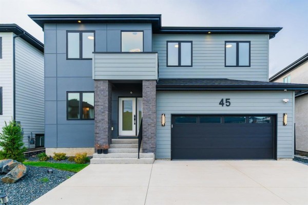 Front facade of a two-story contemporary house with grey siding and a dark garage door. - 45 Karschuk Bay, Winnipeg