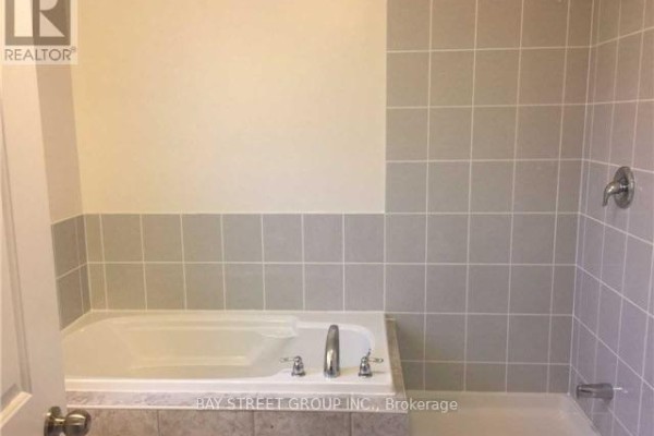Interior view of a bathroom with a large white bathtub surrounded by light gray square tiles. - 45 Longshore Way, Whitby