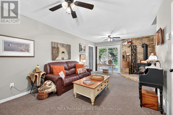 Living room with a brown leather sofa, wooden coffee table, and brick fireplace with wood stove. - 45 Main Street S, Bluewater