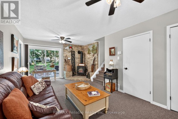 Living room with a brown leather sofa, coffee table, brick fireplace, wood stove, and staircase. - 45 Main Street S, Bluewater