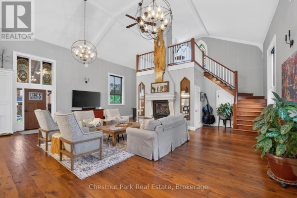 Spacious living room with fireplace, seating area, wood floors, and stairs. - 45 Mcmurray Street, Bracebridge