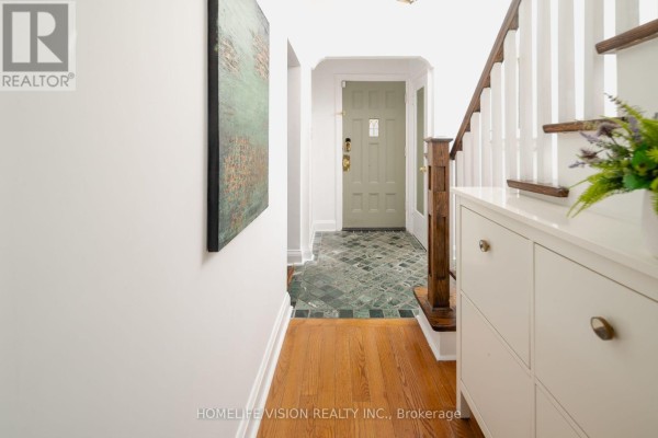 Interior hallway view showing hardwood floors, a white shoe cabinet, a staircase, and a green front door. - 45 Mcrae Drive, Toronto