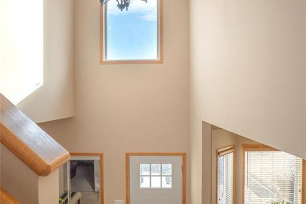 Interior view of a tall foyer with a white front door, a staircase with wooden railings, and a large window. - 45 Moldan Bay, Winnipeg