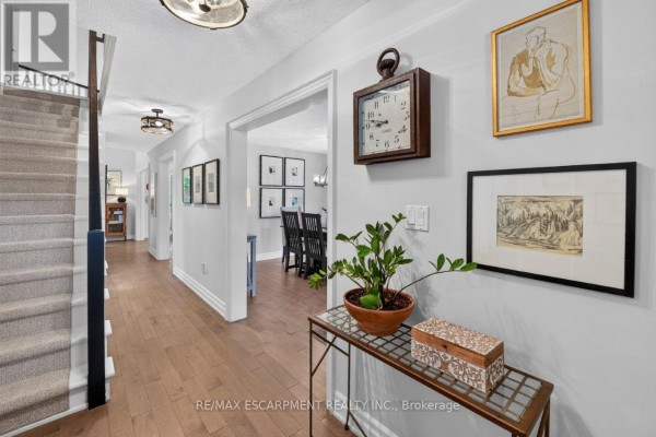 Interior hallway with a staircase, hardwood floors, and a console table with decorative items and artwork on the wall. - 45 Richmond Crescent, Hamilton