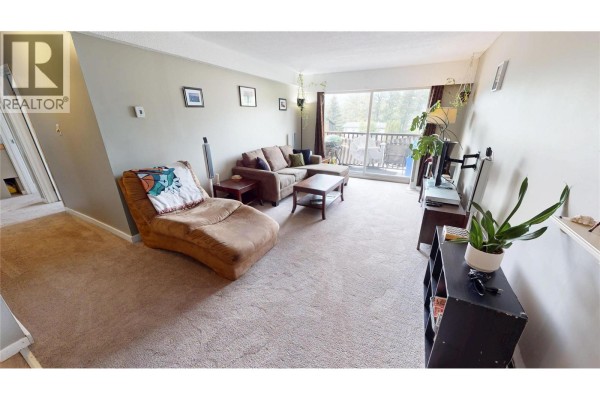 Living room with a sectional sofa, coffee table, armchair, and a large window. - 45 Ridgemont Drive Unit# 302, Fernie