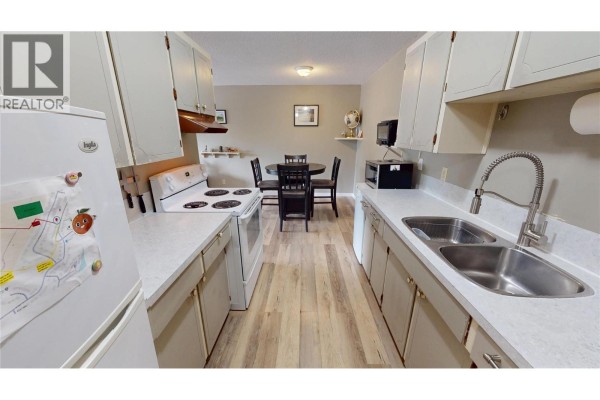 Galley kitchen with white cabinets, a white stove, double sink, and dining area. - 45 Ridgemont Drive Unit# 302, Fernie