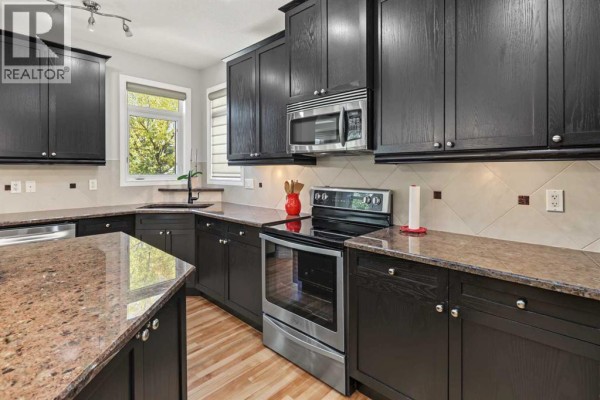 U-shaped kitchen with dark wood cabinets, granite countertops, stainless steel appliances, and a window overlooking the yard. - 45 Royal Oak Manor Nw, Calgary