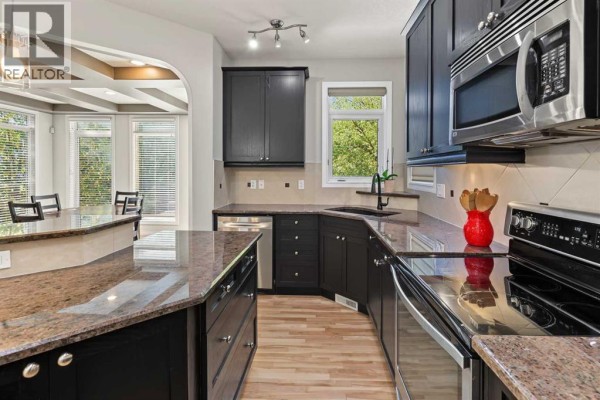 Kitchen with dark wood cabinets, granite countertops, a peninsula, and a breakfast nook with large windows. - 45 Royal Oak Manor Nw, Calgary