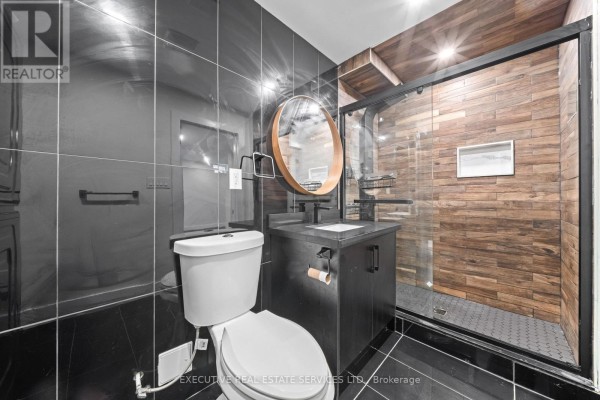 Modern bathroom with wood shower, glass door, vanity, round mirror, and black tile - 45 Sahara Trail Brampton