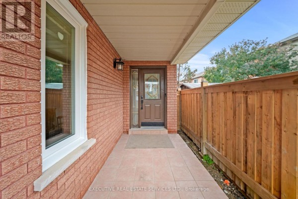 Close-up of the covered front porch entrance with a brown door, brick exterior, and wooden fence. - 45 Sahara Trail, Brampton