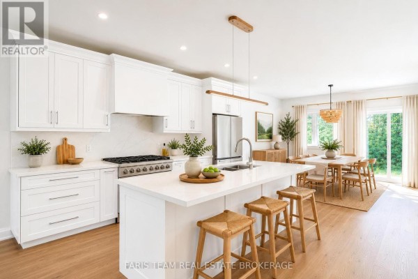 Modern white kitchen with an island, stainless steel appliances, and a dining area beyond. - 45 Sheppard Street, Severn