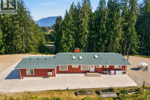 Rear view of the red house with a green roof and a large concrete patio. - 450 20 Avenue Sw, Salmon Arm
