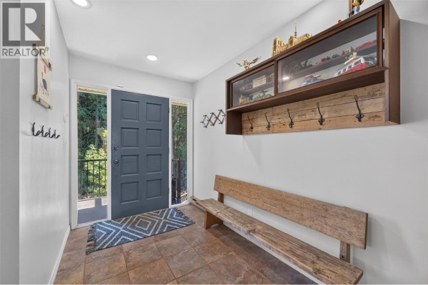 Interior entryway with a grey door, tiled floor, wooden bench, and wall hooks. - 450 20 Avenue Sw, Salmon Arm