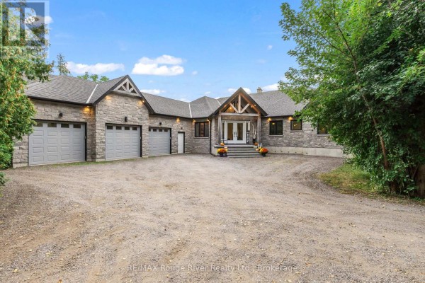 Front exterior of a stone house with a gray roof, featuring a covered porch with double doors and four garage doors. - 4500 Old Scugog Road, Clarington