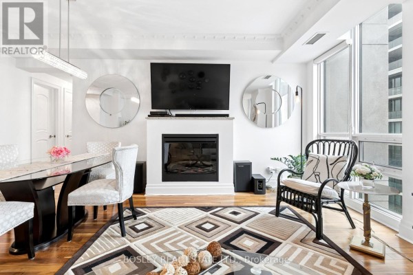 Living and dining area with fireplace, sofa, armchair, patterned rug, and hardwood floors. - 4501 - 16 Harbour Street, Toronto