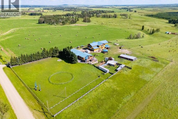 Overhead view of a large yellow house with blue roofs, outbuildings, and fenced paddocks on a green landscape. - 45040 421a Township, Rural Ponoka County