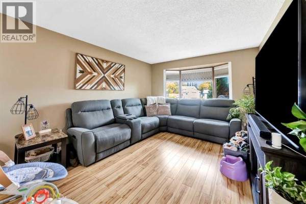 Living room with a grey sectional sofa, bay window, and light wood laminate flooring. - 4505 30a Street Close, Lloydminster