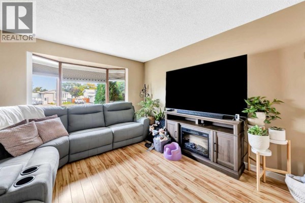 Living room featuring a large grey sectional, electric fireplace media console, and bay window. - 4505 30a Street Close, Lloydminster