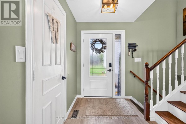 Interior entryway with a white door, wood-look flooring, and a staircase with white railings. - 4505 Susan Drive, Elizabethtown Kitley