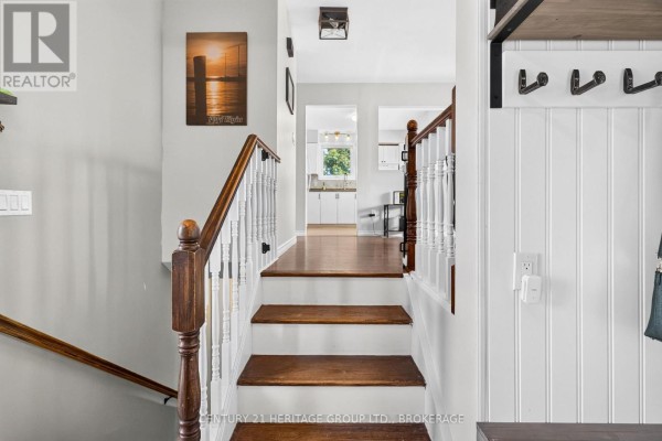 Wooden staircase with white spindles leads to a hallway with a view of the kitchen. - 4505 Susan Drive, Elizabethtown Kitley
