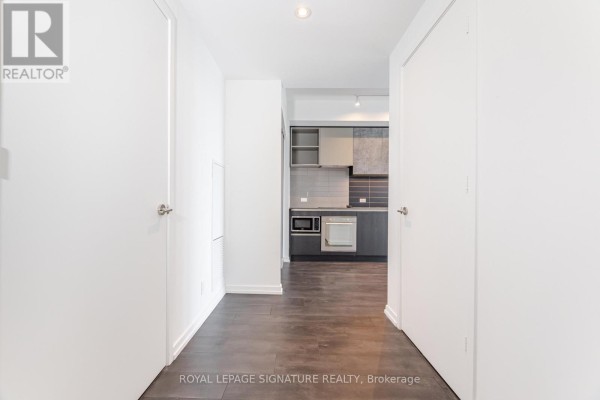 Hallway leading to an open-concept kitchen area with dark wood floors and white doors. - 4508 - 7890 Jane Street, Vaughan