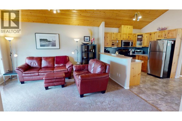 Living room and kitchen area with red sofas, wooden cabinets, and stainless steel appliances. - 451 13th Avenue, Invermere
