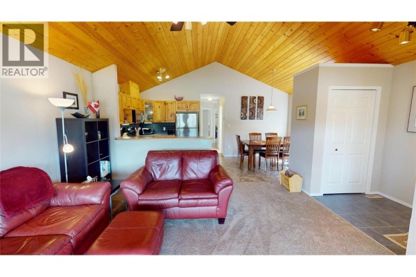 Living and dining area showing red sofas, wooden ceiling, kitchen, and dining table. - 451 13th Avenue, Invermere