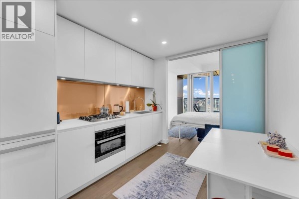 Modern white kitchen with copper backsplash, stainless steel appliances, and a breakfast bar overlooking a bedroom. - 4510 1480 Howe Street, Vancouver