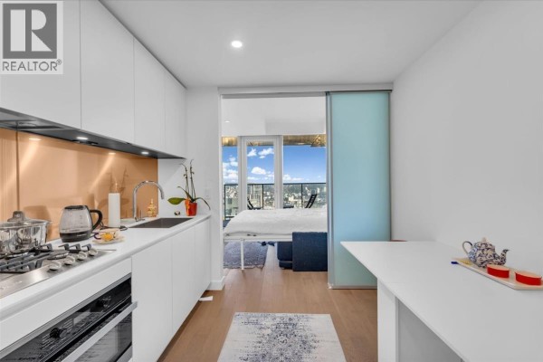 Open-concept studio apartment with a sleek white kitchen, dining area, and view of the city through large windows. - 4510 1480 Howe Street, Vancouver