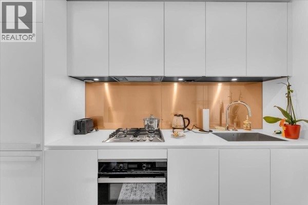 Close-up of a modern kitchen counter with a gas stovetop, sink, copper backsplash, and white cabinetry. - 4510 1480 Howe Street, Vancouver
