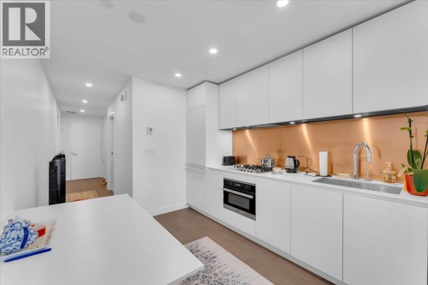 Interior view of a white galley kitchen with a built-in oven and sliding doors leading to the main living area. - 4510 1480 Howe Street, Vancouver