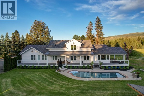 Rear exterior of a white farmhouse with a swimming pool and manicured lawn. - 4510-4520 Stewart Road E, Kelowna