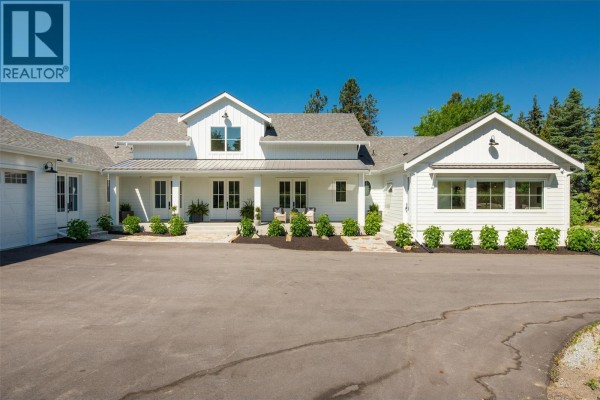 Front entrance of a white farmhouse with a covered porch and double doors. - 4510-4520 Stewart Road E, Kelowna