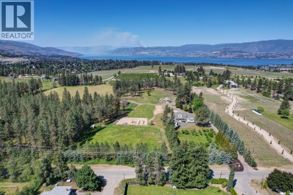 Aerial view of the property showing the farmhouse, vineyard, and distant lake. - 4510-4520 Stewart Road E, Kelowna