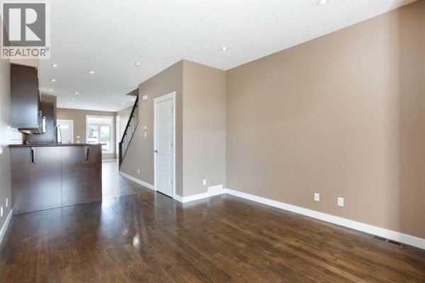 Empty living room with hardwood floors, beige walls, and a view into the kitchen and hallway. - 4510 73 Street Nw, Calgary