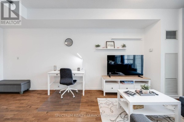 Living room with white desk and chair, media console with television, and grey ottoman. - 4511 - 65 Bremner Boulevard, Toronto