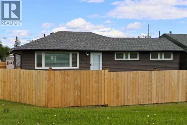 Wooden fence in front of a bungalow with brown siding and a grey roof. - 4511 50 Avenue, Valleyview