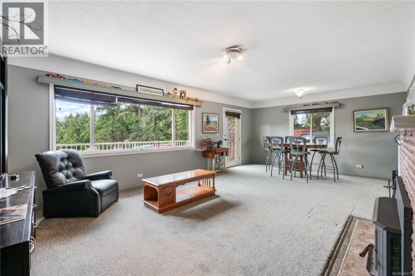 Living and dining area with gray walls, carpet, large windows, and wood furniture. - 4511 Pachena Pl, Saanich