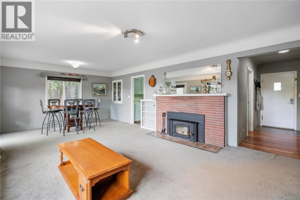 Living room with a brick fireplace, wood floors, gray walls, and dining area. - 4511 Pachena Pl, Saanich