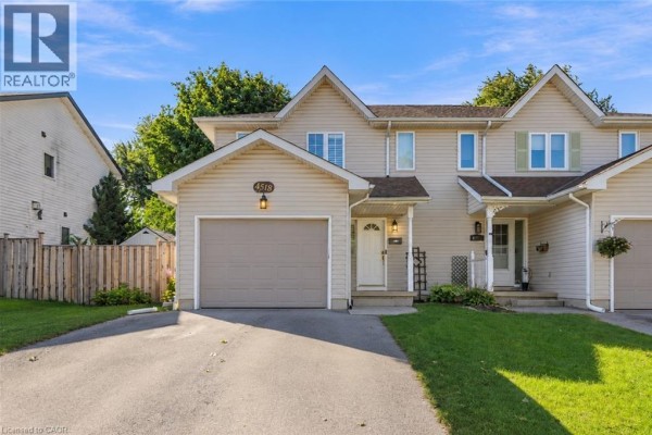 Front exterior of a beige townhouse with a double garage door and green lawn in daylight. - 4518 Garden Gate Terrace, Beamsville