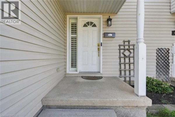 Concrete front porch with a white door, sidelight window, and decorative trellis. - 4518 Garden Gate Terrace, Beamsville