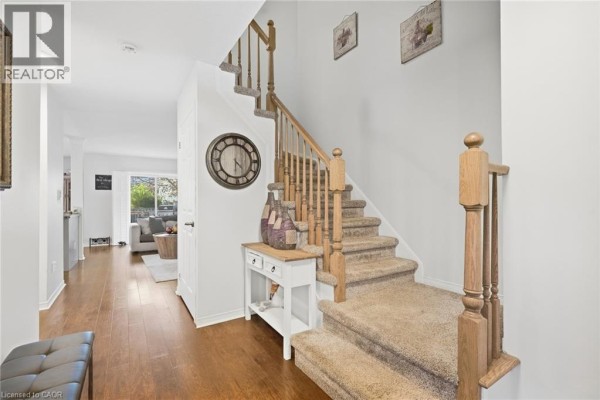Foyer with a carpeted staircase, wood flooring, console table, and a large wall clock. - 4518 Garden Gate Terrace, Beamsville