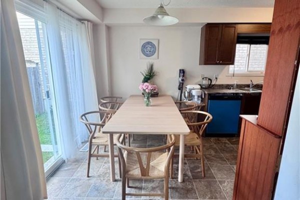 Dining area with a light wood table and six chairs, adjacent to a kitchen with dark wood cabinets. - 452 Beaumont Crescent, Kitchener
