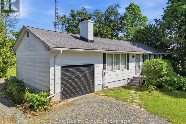 Side view of a white, single-story house with a black garage door and stone pathway. - 452 Marble Point Road, Marmora And Lake