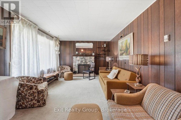 Living room with wood paneling, stone fireplace, large window, and seating. - 452 Marble Point Road, Marmora And Lake