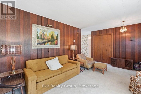 Living room with wood paneling, fireplace, couch, chairs, and double closet doors. - 452 Marble Point Road, Marmora And Lake