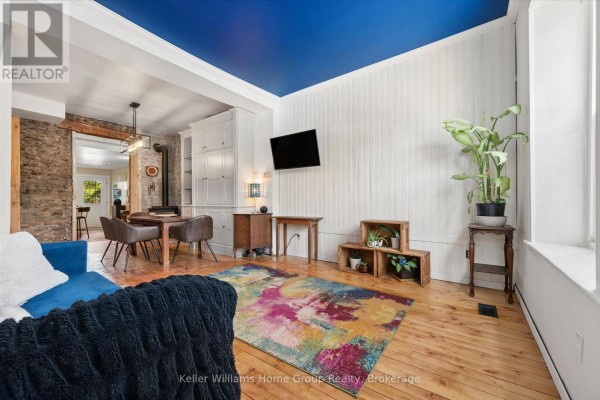 Living and dining area with wood floors, a blue sofa, colorful rug, and exposed brick. - 452 St Andrew Street W, Centre Wellington