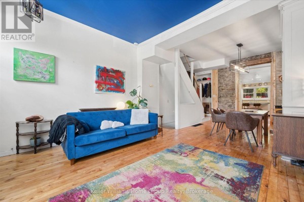 Living area with a blue sofa, abstract art, wood floors, and a view into the dining area. - 452 St Andrew Street W, Centre Wellington
